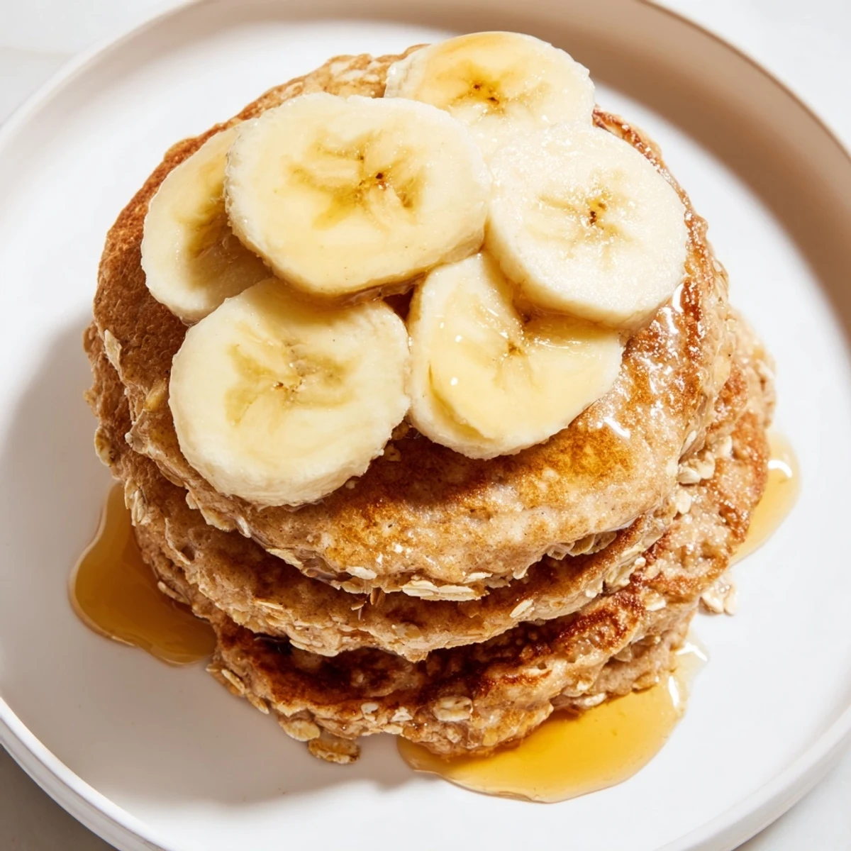 Freshly made banana oat pancakes, drizzled with sweet maple syrup, perfect for a weekend treat.