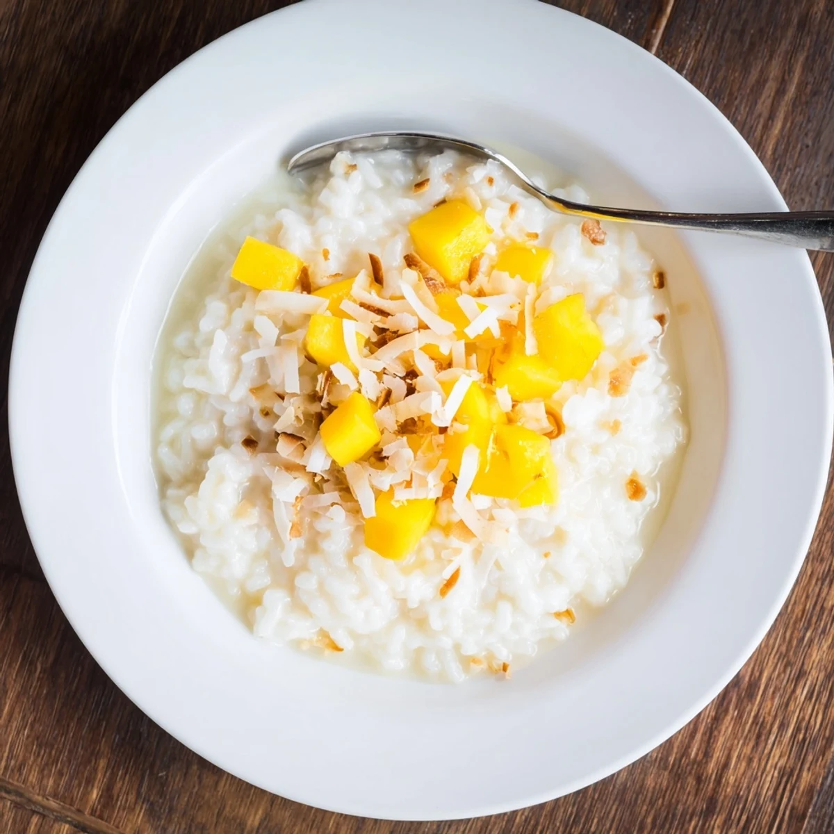 Overhead view of a plate of Coconut Rice Sweet, steaming beside tropical fruit and a drizzle of sweetened coconut cream.