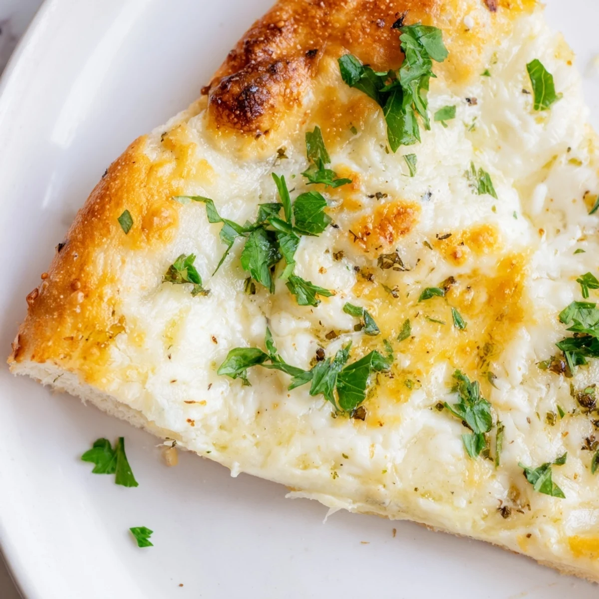 Thick crust of Creamy Garlic White Pizza shows garlic cream sauce and melted cheese.