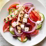 This Greek salad with grilled chicken showcases juicy chicken atop vibrant vegetables, drizzled with olive oil dressing.
