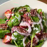 A close-up view of the delicious strawberry spinach salad with glistening poppy seed dressing and red onion.
