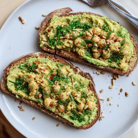 Creamy avocado toast with chickpeas and herbs, a colorful breakfast with rustic, toasted bread.
