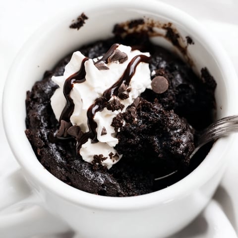 A close-up of a warm, fudgy Oreo Mug Cake topped with whipped cream, ready to eat.
