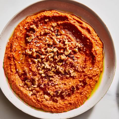 Smoky Syrian muhammara dip, a vibrant red color, served with pita bread and drizzled olive oil.
