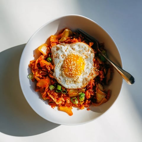 A vibrant bowl of Kimchi Fried Rice topped with a sunny-side-up egg and sesame seeds, showcasing caramelized kimchi and colorful vegetables.