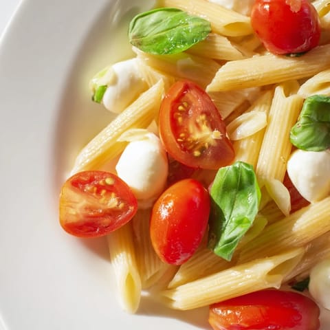 Shallow bowl of vibrant Caprese Salad Pasta featuring juicy tomatoes, creamy mozzarella, and fragrant basil, served as a light, vegetarian main dish with a drizzle of olive oil.