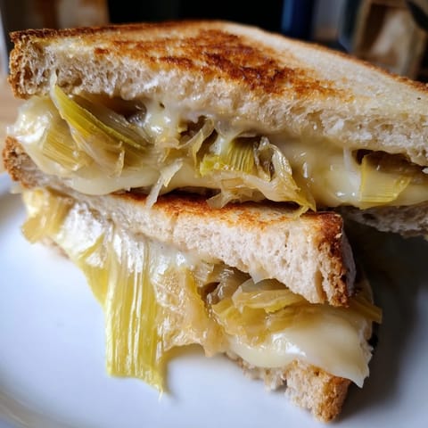 A close-up of Havarti & Caramelized Leek Grilled Cheese with melty cheese oozing between golden-brown bread slices.