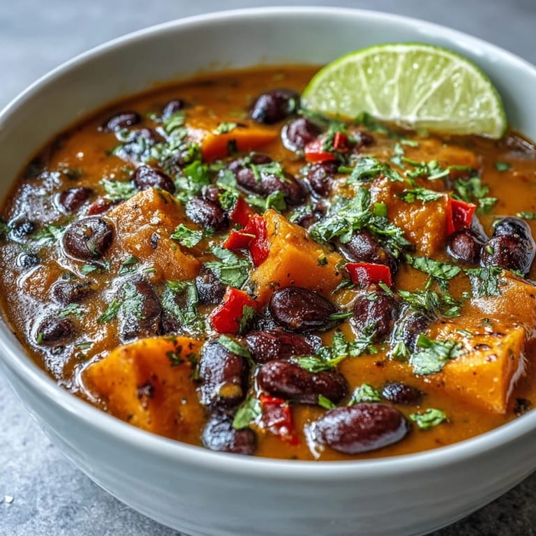 Bright, colorful Sweet Potato and Black Bean Soup in a white bowl, featuring diced vegetables and beans in a rich broth.